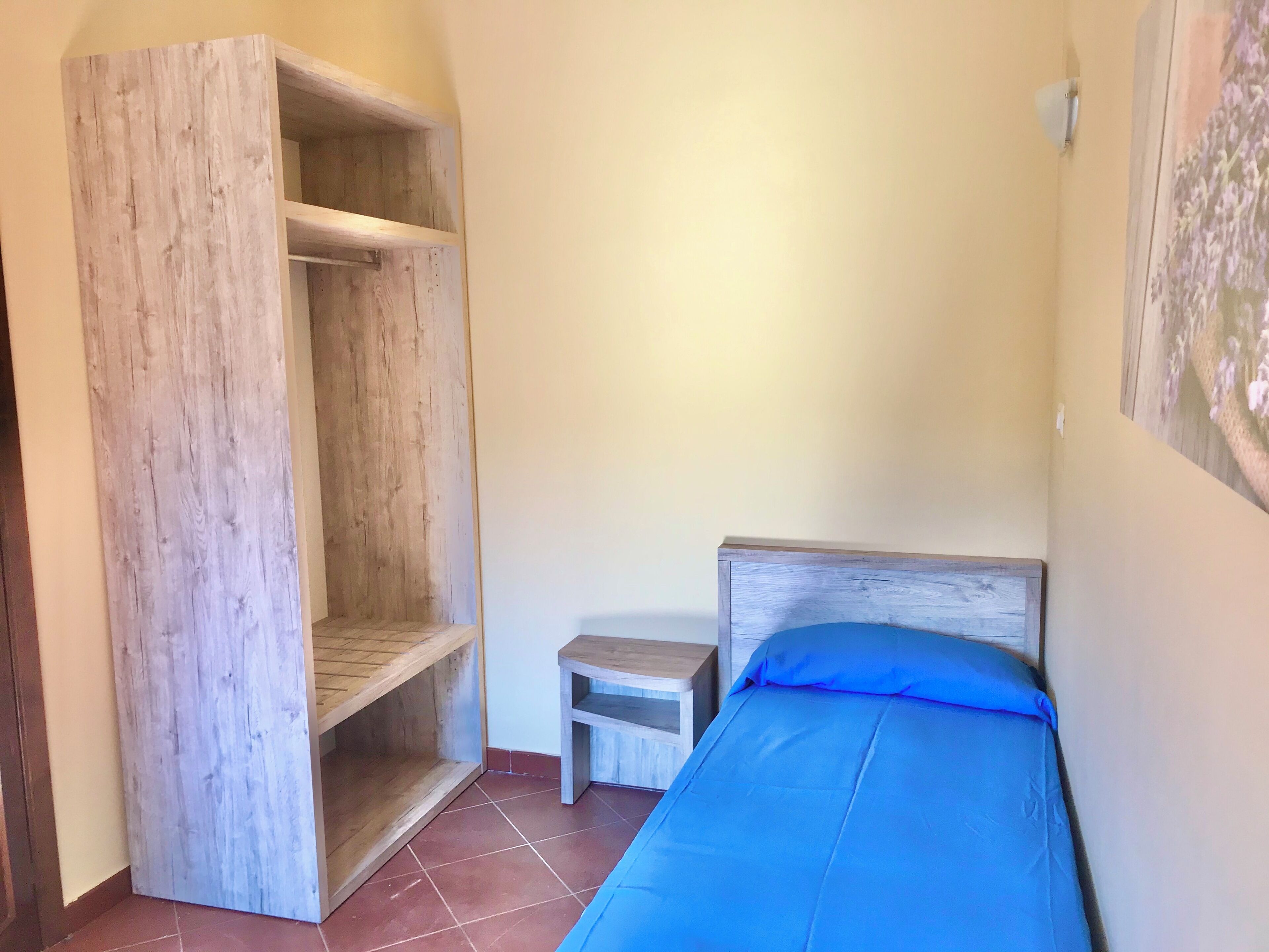 A small room with a bed, a wooden wardrobe, and a small table.