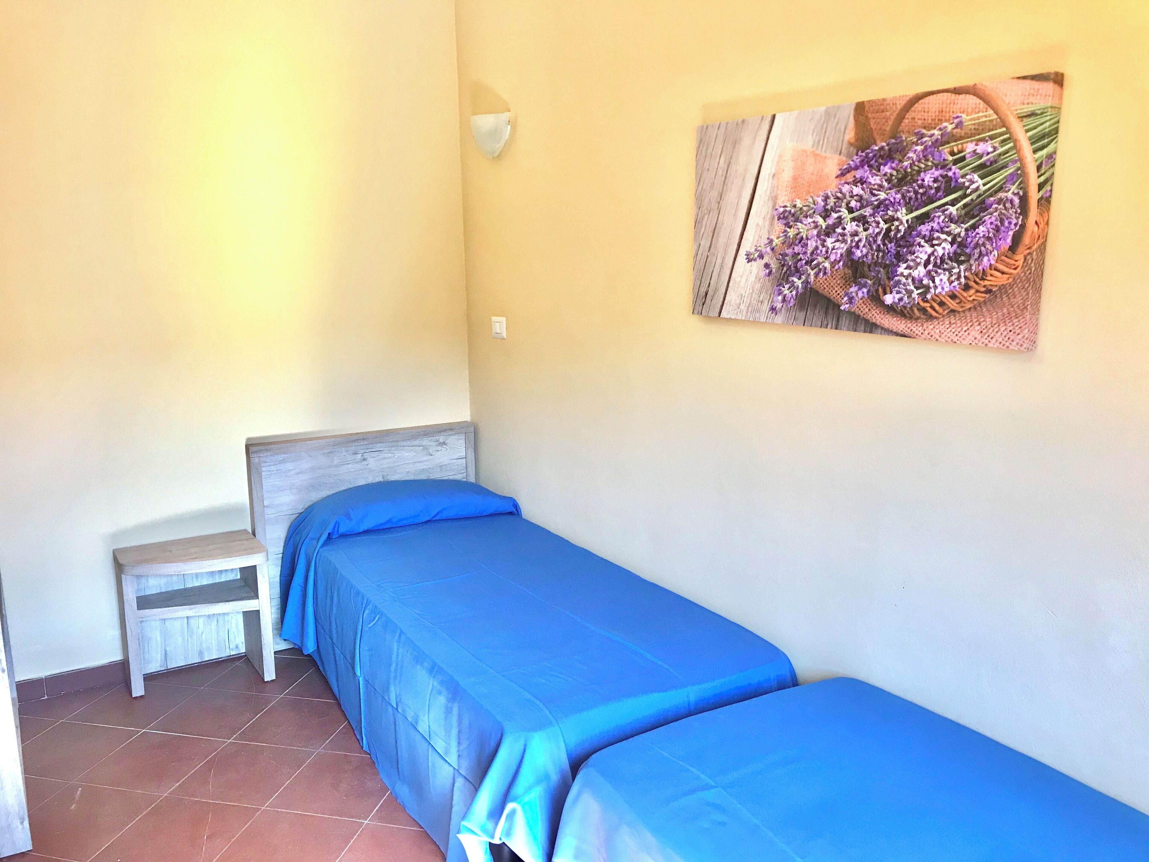 A small, single-bed room with a wooden headboard, a bench, and a wall-mounted light fixture.