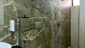 A bathroom with marble walls, a white toilet, a sink, and a shower. - B&B Estrella Hotel And Resort  (Indore)