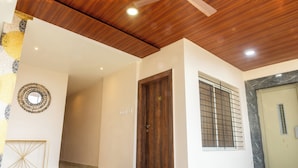 A hallway with a wooden ceiling, a marble floor, a wooden door, and a window with bars. - B&B Estrella Hotel And Resort  (Indore)