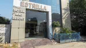 The exterior of Estrella Hotel and Resort with a glass entrance and a blue fence. - B&B Estrella Hotel And Resort  (Indore)