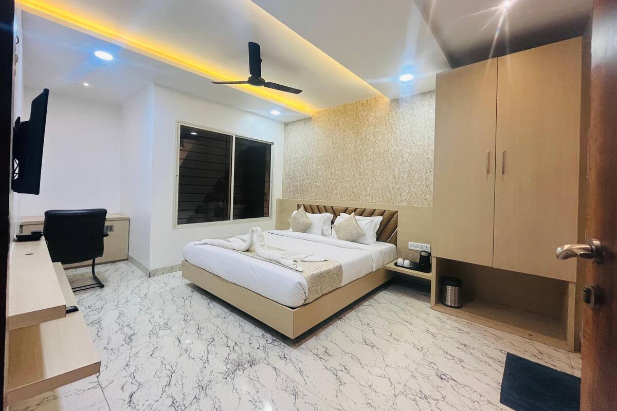 A modern bedroom with a large bed, a desk, a chair, a wardrobe, and a ceiling fan.