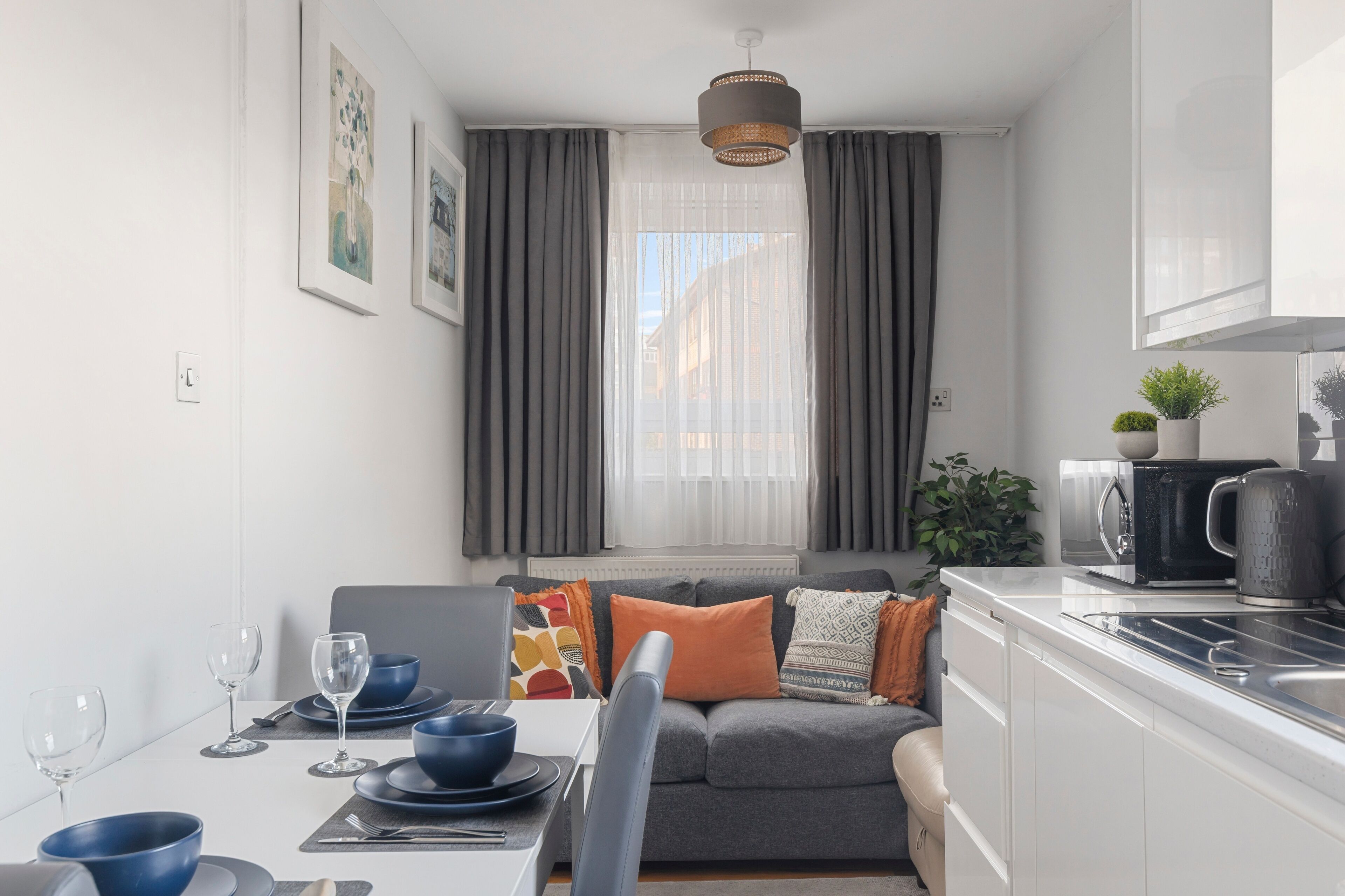 Eine moderne Küche mit Essbereich, grauem Sofa und einem Fenster mit Vorhängen.