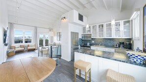 A modern kitchen with white cabinetry, a large island, and a dining area with a wooden table and wicker chairs.