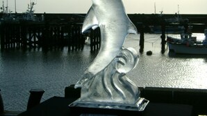 Eine Delfin-Skulptur in einem Hafen mit Booten und Stegen im Hintergrund.