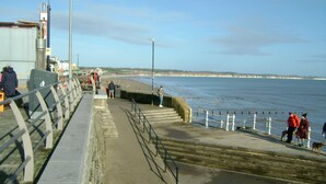 Eine Küstenpromenade mit Betonweg, Metallgeländern und Blick auf das Meer.