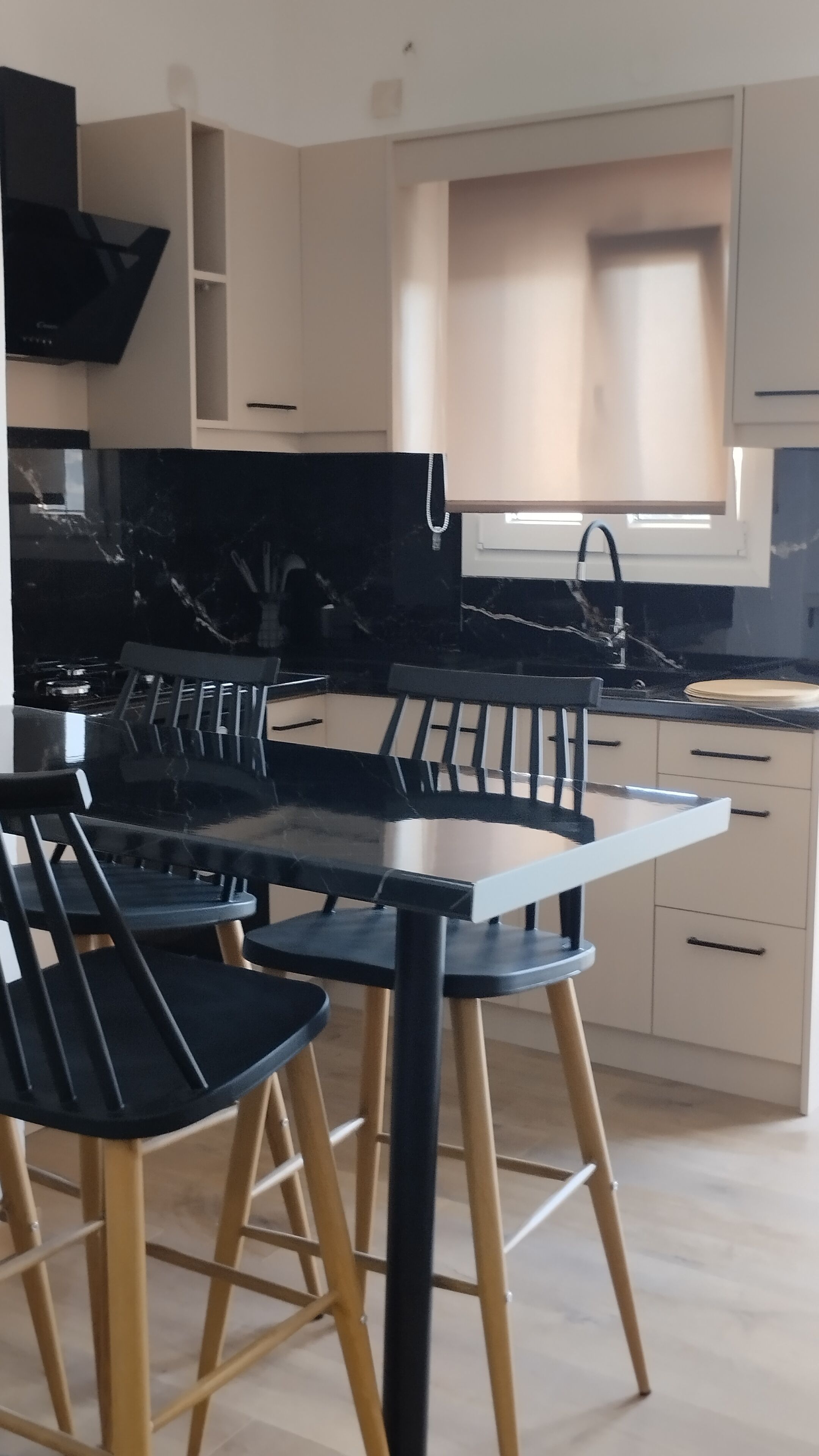 A modern kitchen with a black marble countertop, wooden chairs, and light-colored cabinets.