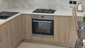 A modern kitchen with white cabinets, a built-in oven, a gas stove, and a coffee maker. - INAS 2 BEDROOM APARTMENTS (Corfu)
