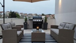 A rooftop patio with wicker furniture, a glass-top coffee table, and a barbecue grill. - INAS 2 BEDROOM APARTMENTS (Corfu)