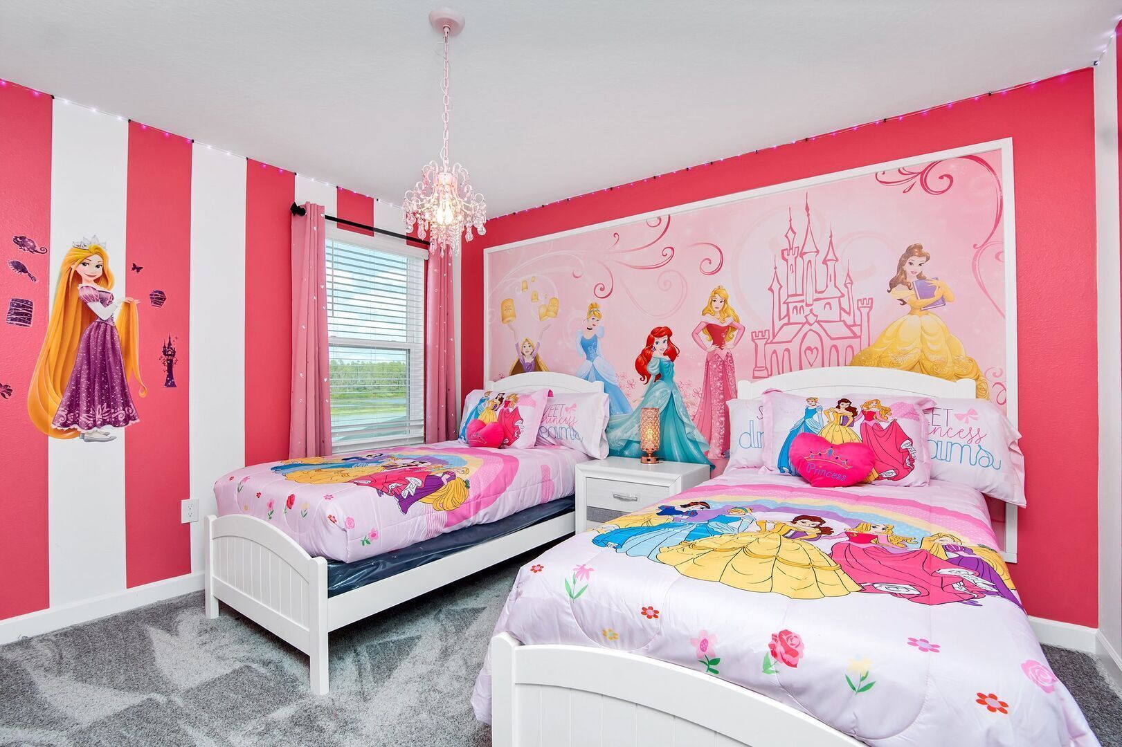 A pink-themed bedroom with two beds, a chandelier, and Disney princess decorations.