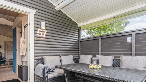 A covered patio area with a dark-colored wicker sofa and a matching table, number 57 displayed on the wall, and a clear view of the outside. - 4 Star Holiday Home in Hovborg (Hovborg)