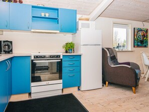 A compact kitchen with blue cabinets, a white refrigerator, a microwave, and a stove. There's a small plant on the counter and a chair in the corner. - 4 Star Holiday Home in Hovborg (Hovborg)