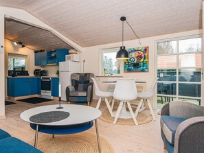 A modern kitchen with blue cabinets, a dining area with white chairs, and a colorful painting on the wall. - 4 Star Holiday Home in Hovborg (Hovborg)