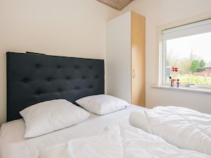 A bedroom with a large bed, a dark headboard, and a window with a view of a house and trees. - 4 Star Holiday Home in Hovborg (Hovborg)