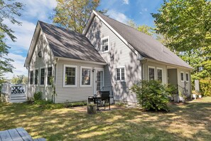 A two-story house with a front porch, a grill, and a small garden area. - Lake Winnipesaukee Waterfront Home Private Beach Dock Sleeps 10 Sunset Views (Moultonborough)