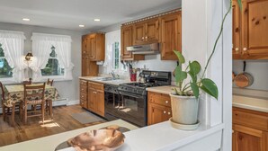 A modern kitchen with wooden cabinets, stainless steel appliances, and a dining area with a table and chairs. - Lake Winnipesaukee Waterfront Home Private Beach Dock Sleeps 10 Sunset Views (Moultonborough)