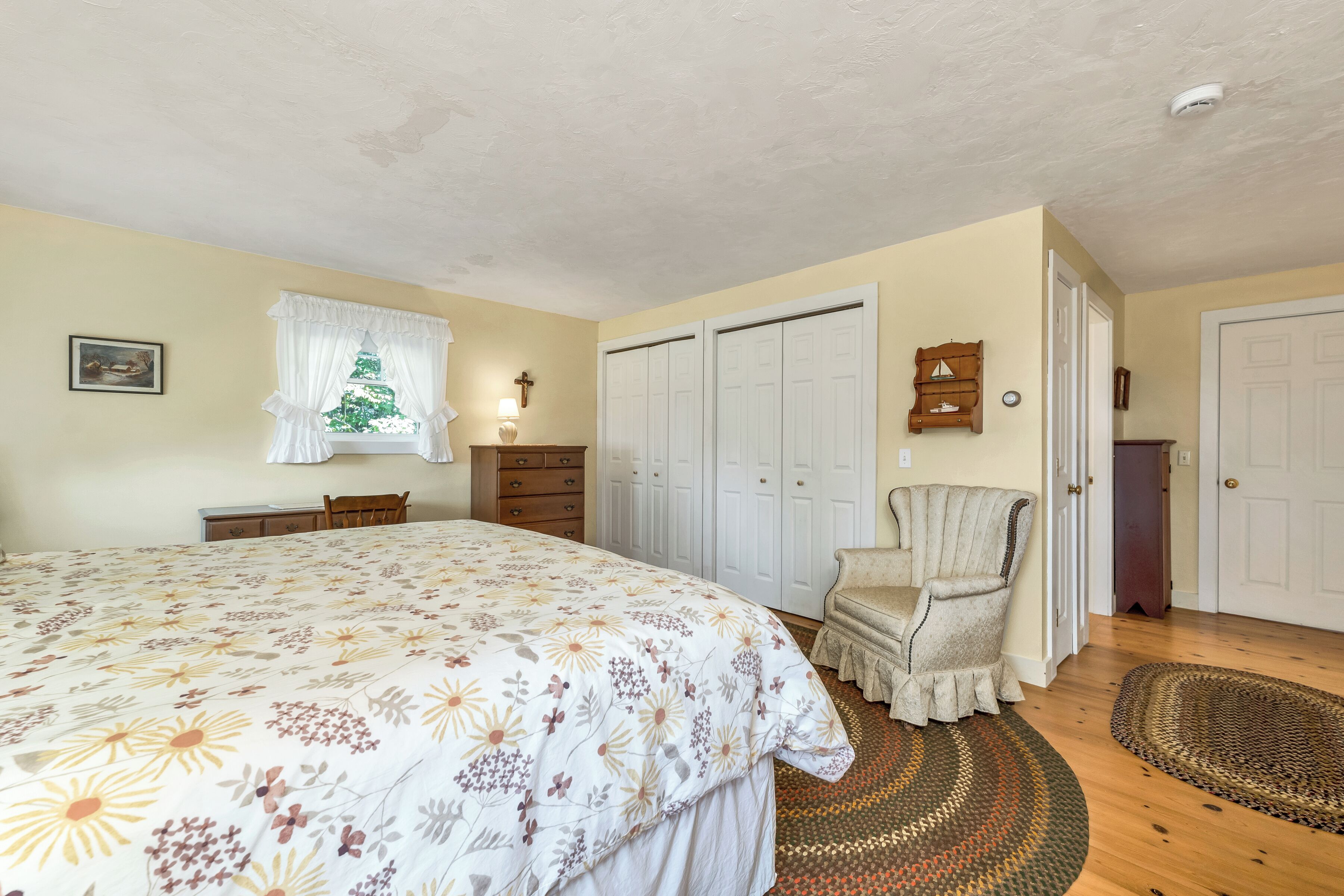 Une chambre avec un grand lit, une chaise, une armoire et une petite table.