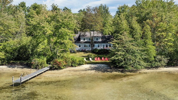 A house surrounded by dense trees, a dock, and a clear view of the property. - Lake Winnipesaukee Waterfront Home Private Beach Dock Sleeps 10 Sunset Views (Moultonborough)