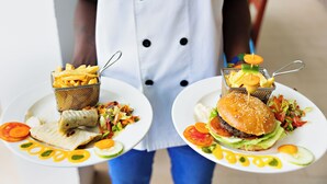 Une personne tenant deux assiettes : sur la première, on voit un hamburger et des frites, et sur la deuxième, un sandwich et une salade.