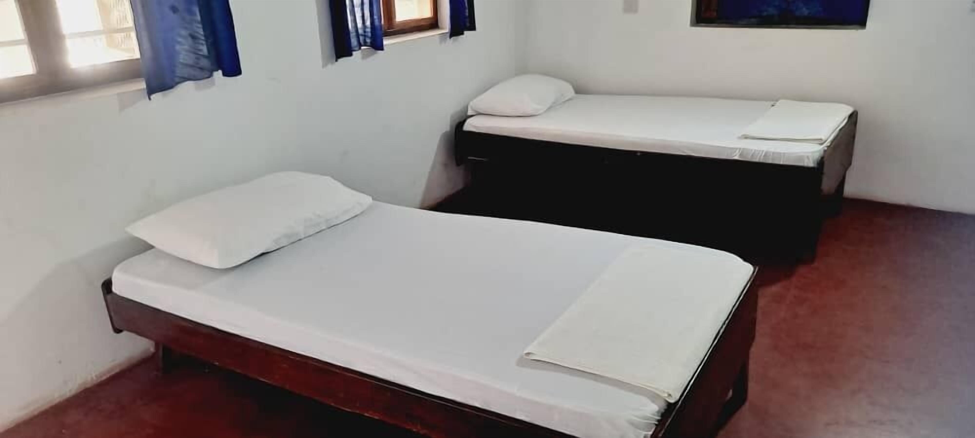 Een kamer met twee eenpersoonsbedden, een raam met gordijnen en een klein tafeltje.