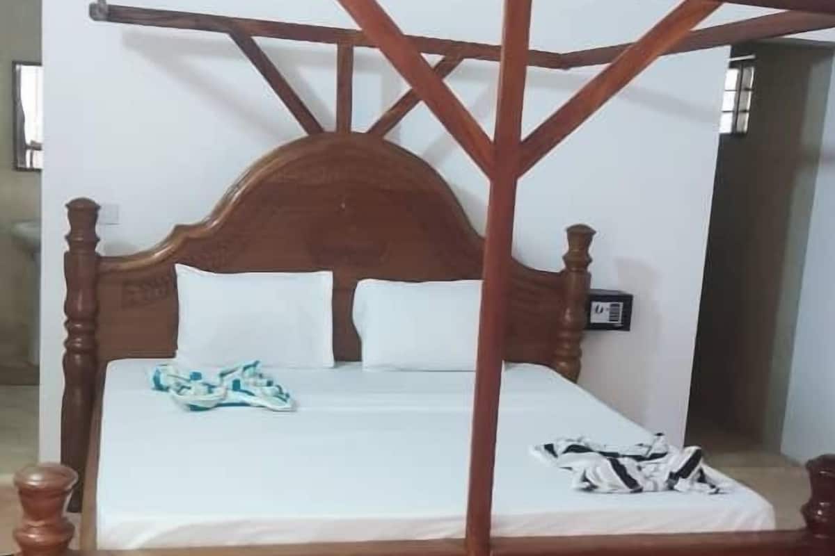 A wooden four-poster bed with a white mattress and pillows, a wooden headboard, and a ceiling fan.