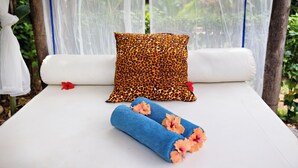 Un lit avec du linge de lit blanc, un coussin à motifs léopard et une serviette bleue ornée de fleurs.
