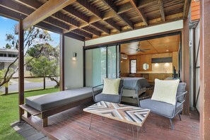 A modern outdoor seating area with a wooden deck, two grey sofas with patterned cushions, and a wooden table.