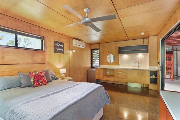 A modern bedroom with a large bed, a ceiling fan, a built-in wardrobe, and a bathroom with a mirror and sink.