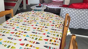 A cozy room with a bed, a table with a colorful tablecloth, a red wall, a staircase, and a television mounted on the wall. - Charming fisherman's cottage (Île-de-Sein)