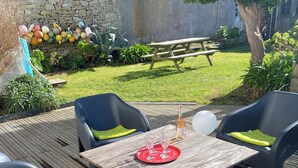 An outdoor patio with a wooden table and four chairs, a bottle of wine, and a tray with glasses. - Charming fisherman's cottage (Île-de-Sein)