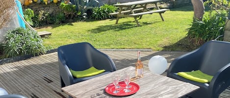 En udendørs terrasse med et træbord og fire stole, en vinflaske og et fad med glas.