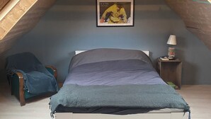 A bedroom with a sloped ceiling, a bed, a chair, a nightstand with a lamp, and a framed picture on the wall. - Charming fisherman's cottage (Île-de-Sein)