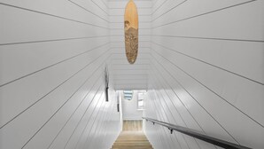 A staircase with wooden steps and white walls, leading to a landing with a surfboard decoration.