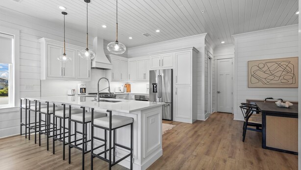 A modern kitchen with white cabinetry, a large island with bar stools, stainless steel appliances, and pendant lighting.
