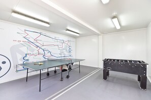 A room with a foosball table and a ping pong table, both with wheels.