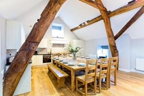 Een ruime keuken met houten balken, een eettafel gedekt voor zes personen, en een groot raam dat natuurlijk licht binnenlaat.