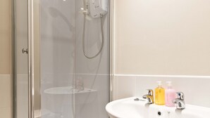 Une douche fermée par des parois en verre, dotée d’un pommeau de douche à main et d’un robinet fixé au mur.