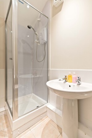 A glass-enclosed shower with a handheld showerhead and a wall-mounted faucet.