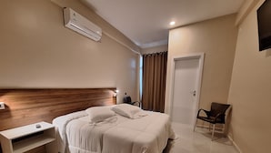 Ein modernes Hotelzimmer mit einem großen Bett, einem Nachttisch, einer Klimaanlage, einem Sessel und einer Tür.