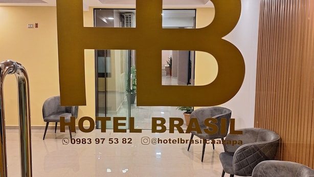 Eine moderne Hotelhalle mit einem großen 'HB'-Schild, einer Rezeption und mehreren grau gepolsterten Sesseln.