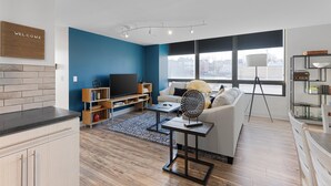 Ein modernes Wohnzimmer mit blauer Akzentwand, einer Couch, einem Couchtisch, einem Fernseher und einem Bücherregal.