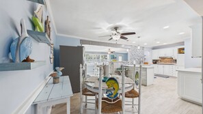 A modern kitchen with white cabinetry, a central island, and a dining area with a white table and chairs.