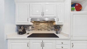 Una cocina con gabinetes blancos, extractor de acero inoxidable, salpicadero de azulejos y un juego de cuchillos.