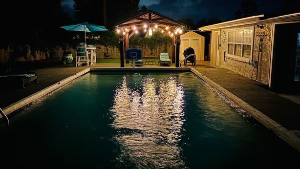 Ein Schwimmbecken bei Nacht mit einem Pavillon und Sitzbereich im Freien.