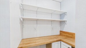 A kitchen with white cabinetry, a wooden countertop, and two white shelves.