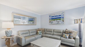A living room with a grey leather sofa, a white coffee table, a lamp, and two paintings on the wall.