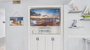 A flat-screen TV mounted on a wall above a white cabinet, with a beach scene on the screen. - Happy OURS 206–Pool Near Beach–Sleeps 6 (Panama City Beach)