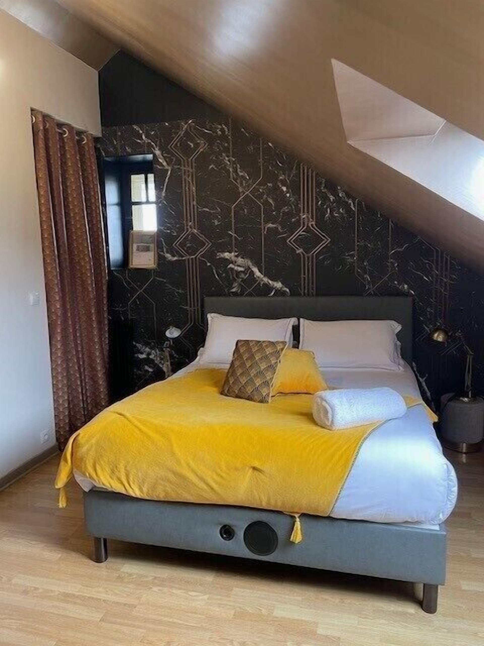 Une chambre à coucher avec un lit, une fenêtre, un rideau et un mur orné d’un motif géométrique.