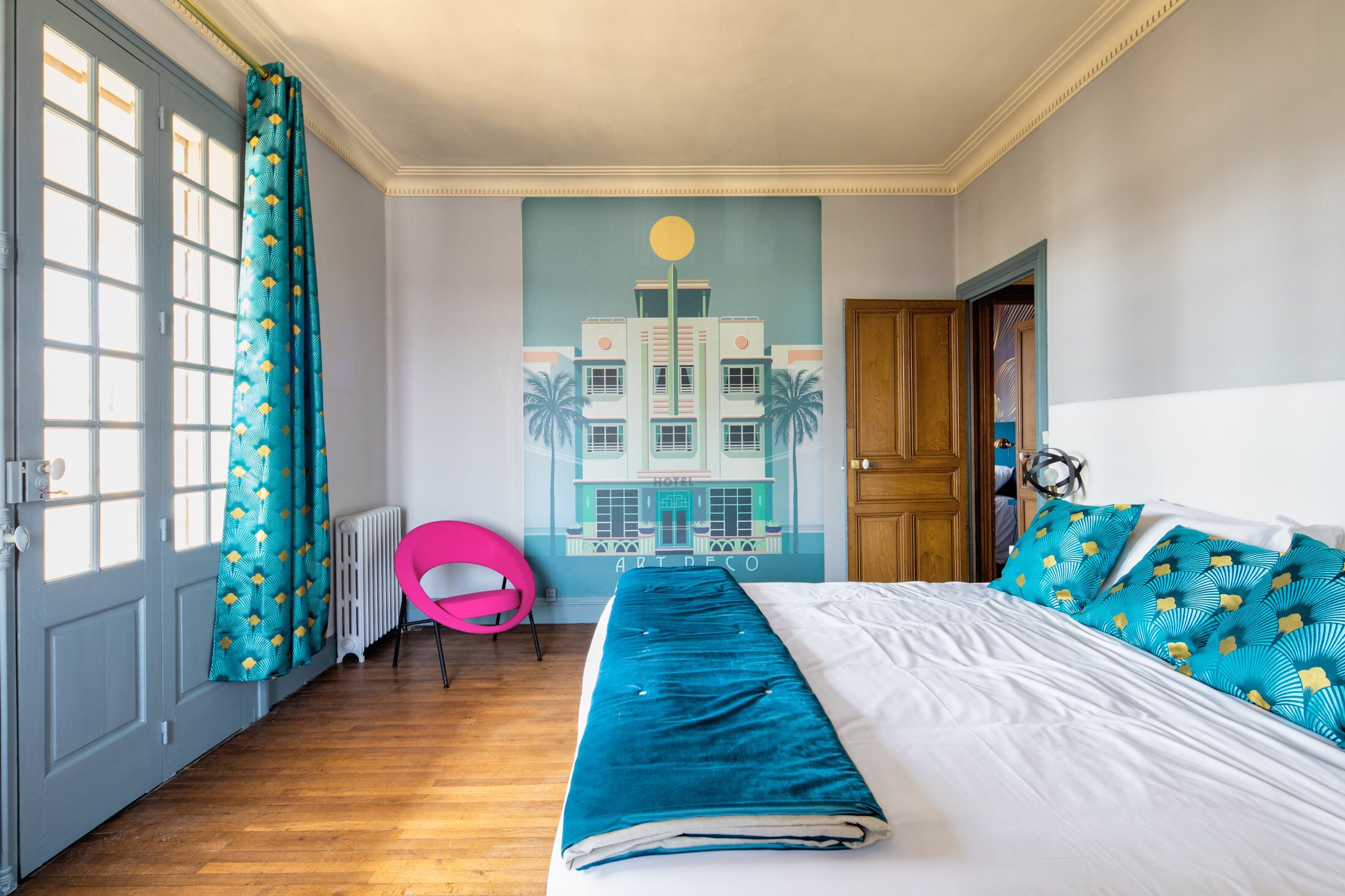 Une chambre d’hôtel avec un lit, une grande fenêtre avec des rideaux, un radiateur et une fresque murale.