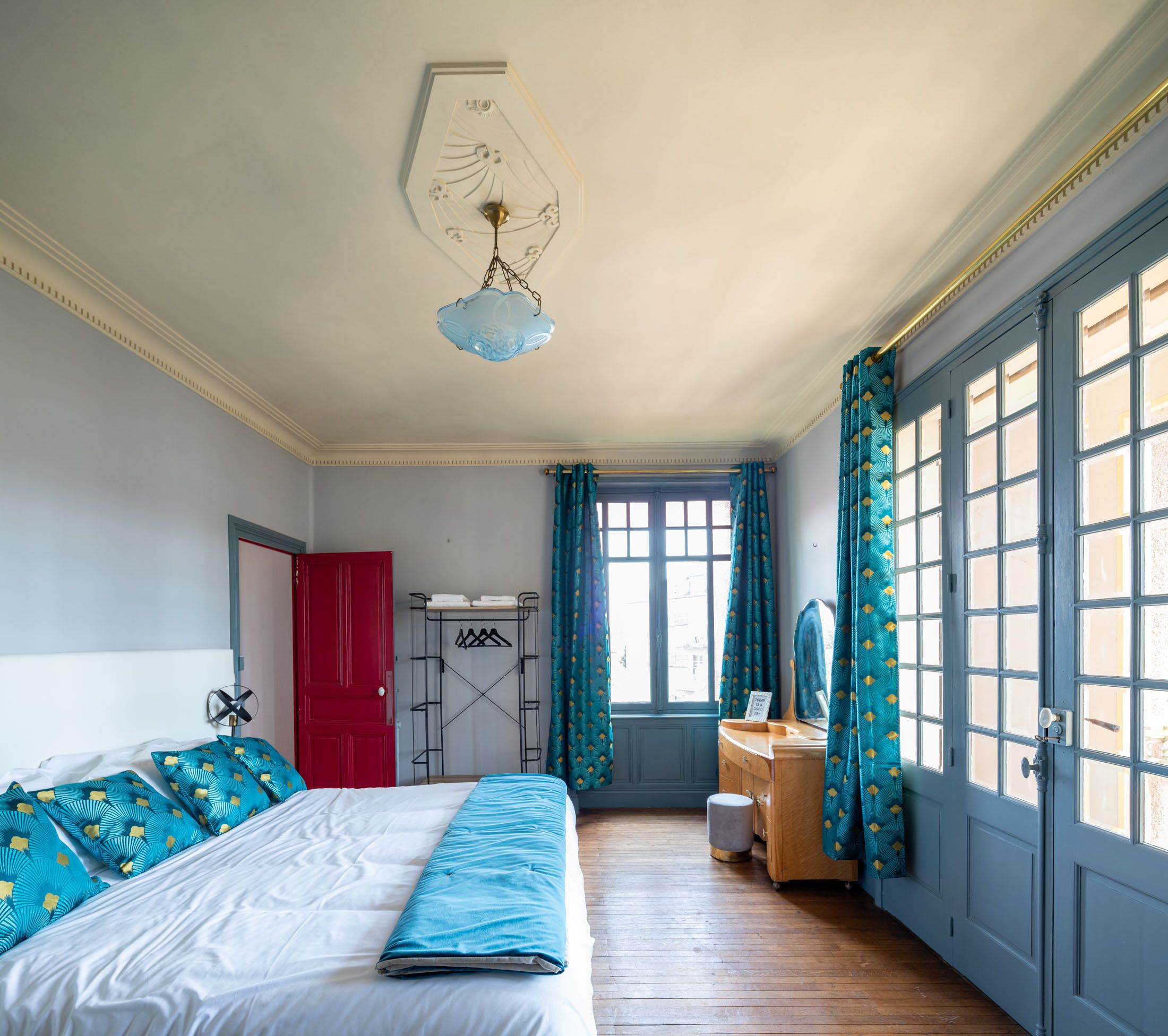 Une chambre à coucher comprenant un lit, une commode, un miroir, une armoire et une fenêtre avec des rideaux.